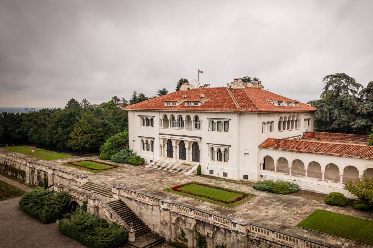 A historic white villa set amid manicured gardens in Belgrade's leafy Dedinje district.