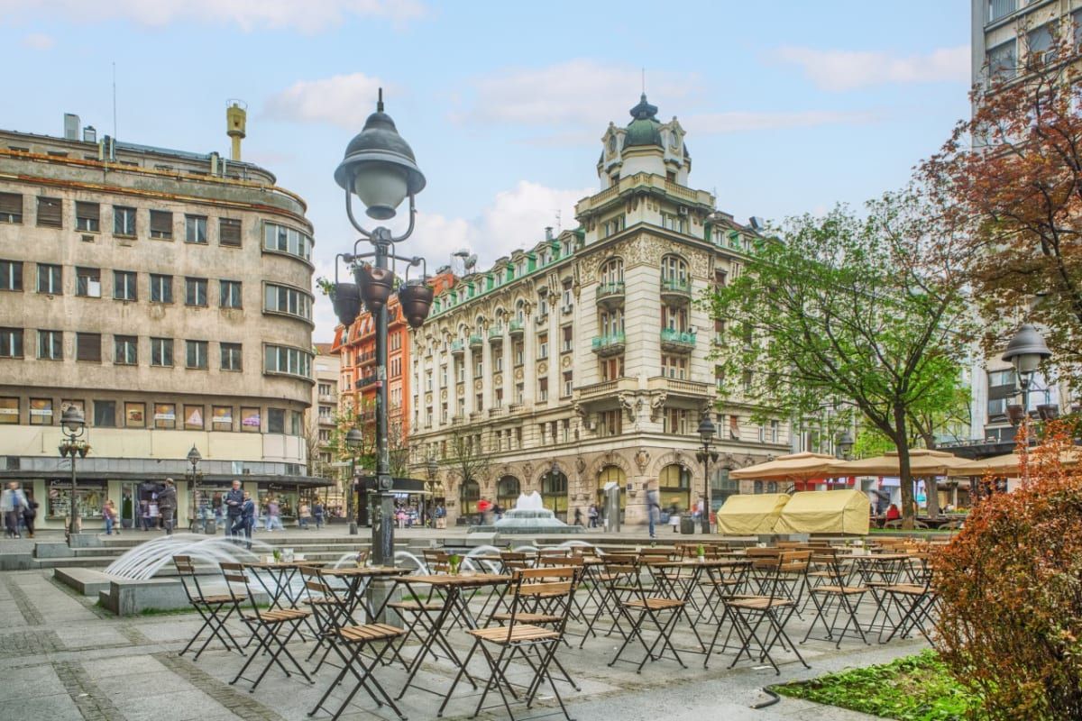 Café tables on a leafy central Belgrade square framed by ornate early-1900s façades near Dorćol.