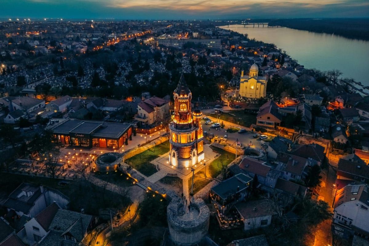 The Gardoš Tower lit at twilight above Zemun's old rooftops beside the Danube.