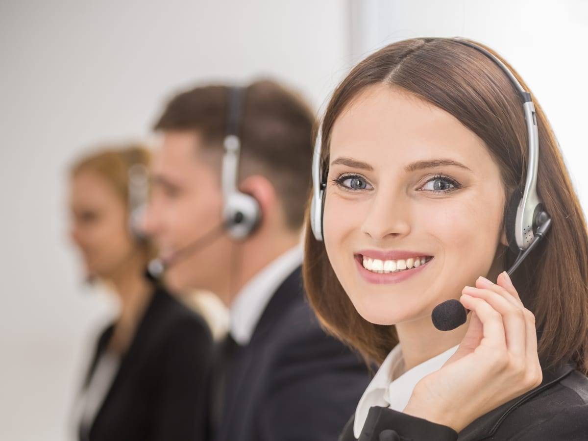 A smiling relocation consultant wearing a headset, with two colleagues taking calls behind her