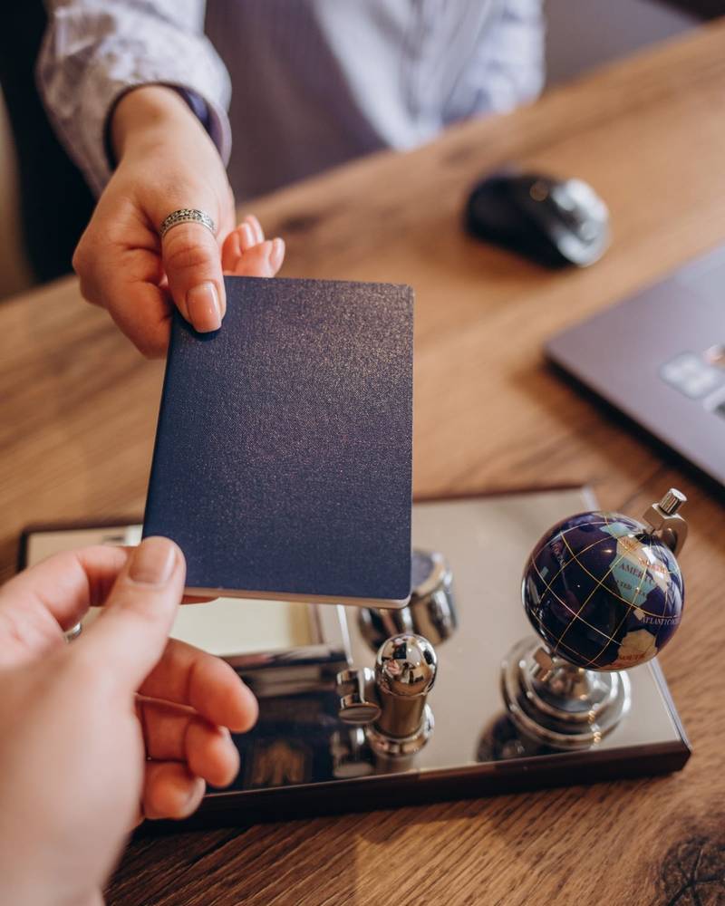 Ein Reisepass wird über einen Schreibtisch gereicht, neben einem amtlichen Stempel und einem kleinen Globus