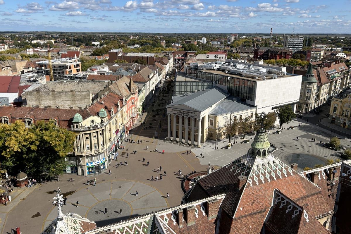 Aerial view over Subotica's main square and pedestrian zone, the National Theatre and ornate City Hall rooftops in the foreground.