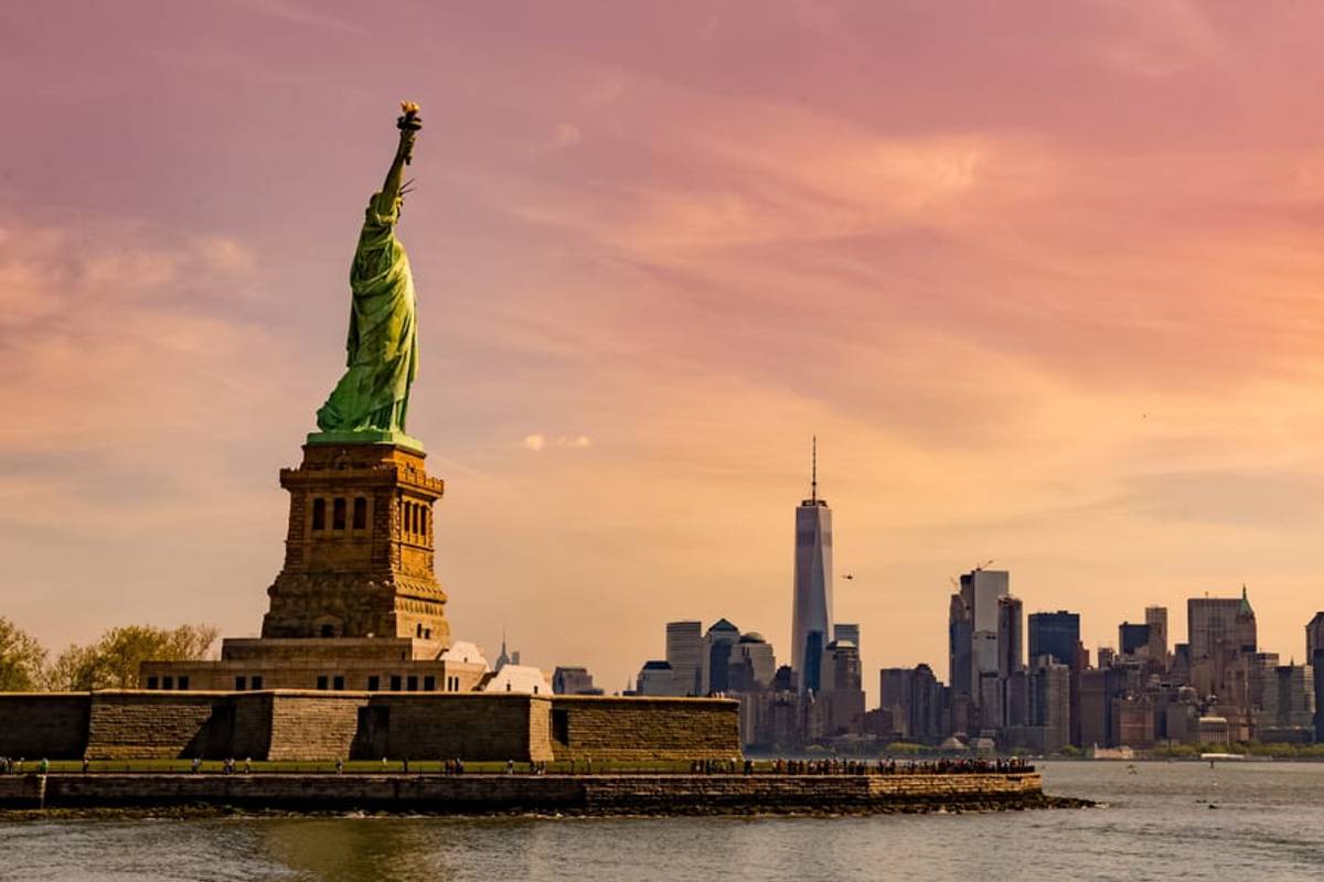 The Statue of Liberty with the Lower Manhattan skyline at sunset, New York, United States