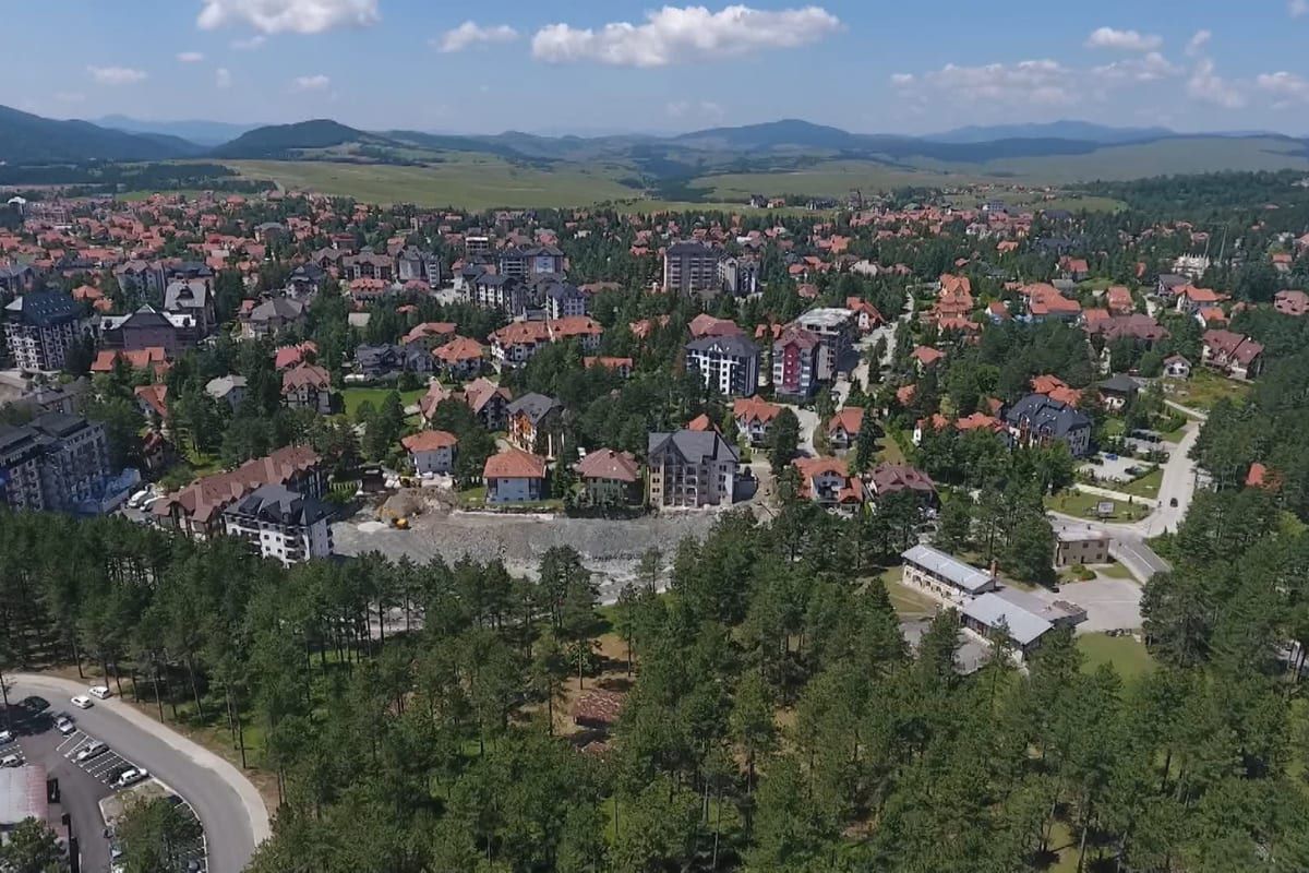 An aerial view of red-roofed houses and apartment blocks set among pine forest in the Zlatibor and Čajetina built-up area.