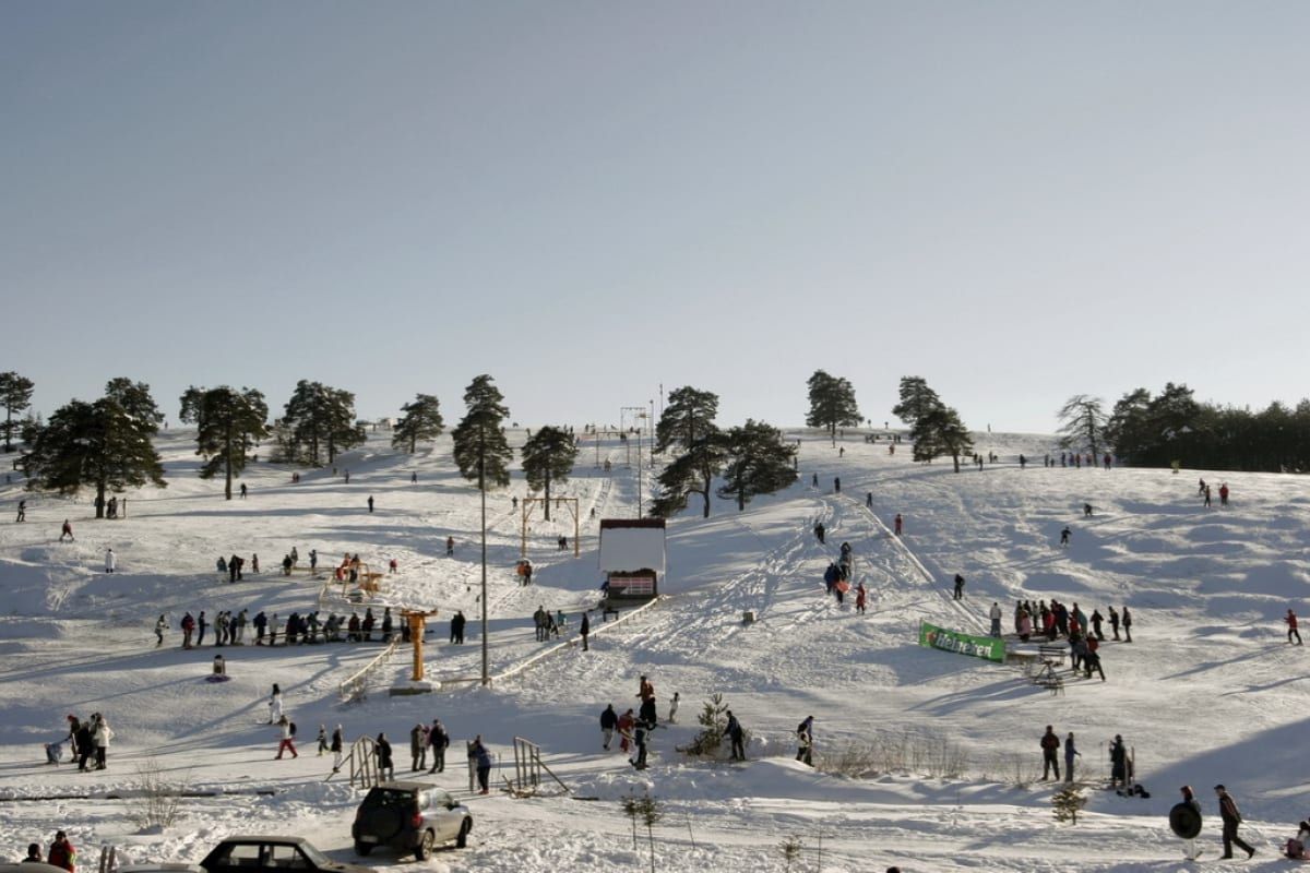 People on the snowy Obudovica ski slope above Zlatibor's centre in winter, with a ski lift and pine trees.