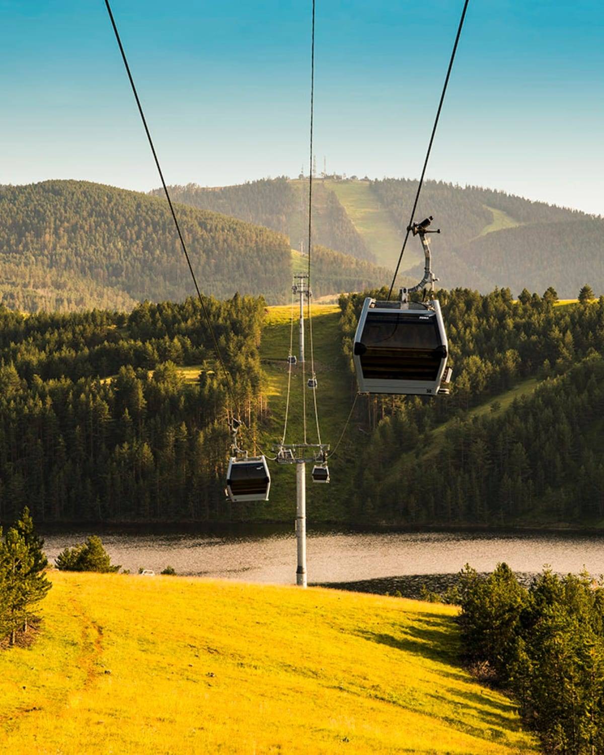 Die Gondelkabinen der Gold-Gondola über grünen Hügeln und einem See, Zlatibor, Serbien