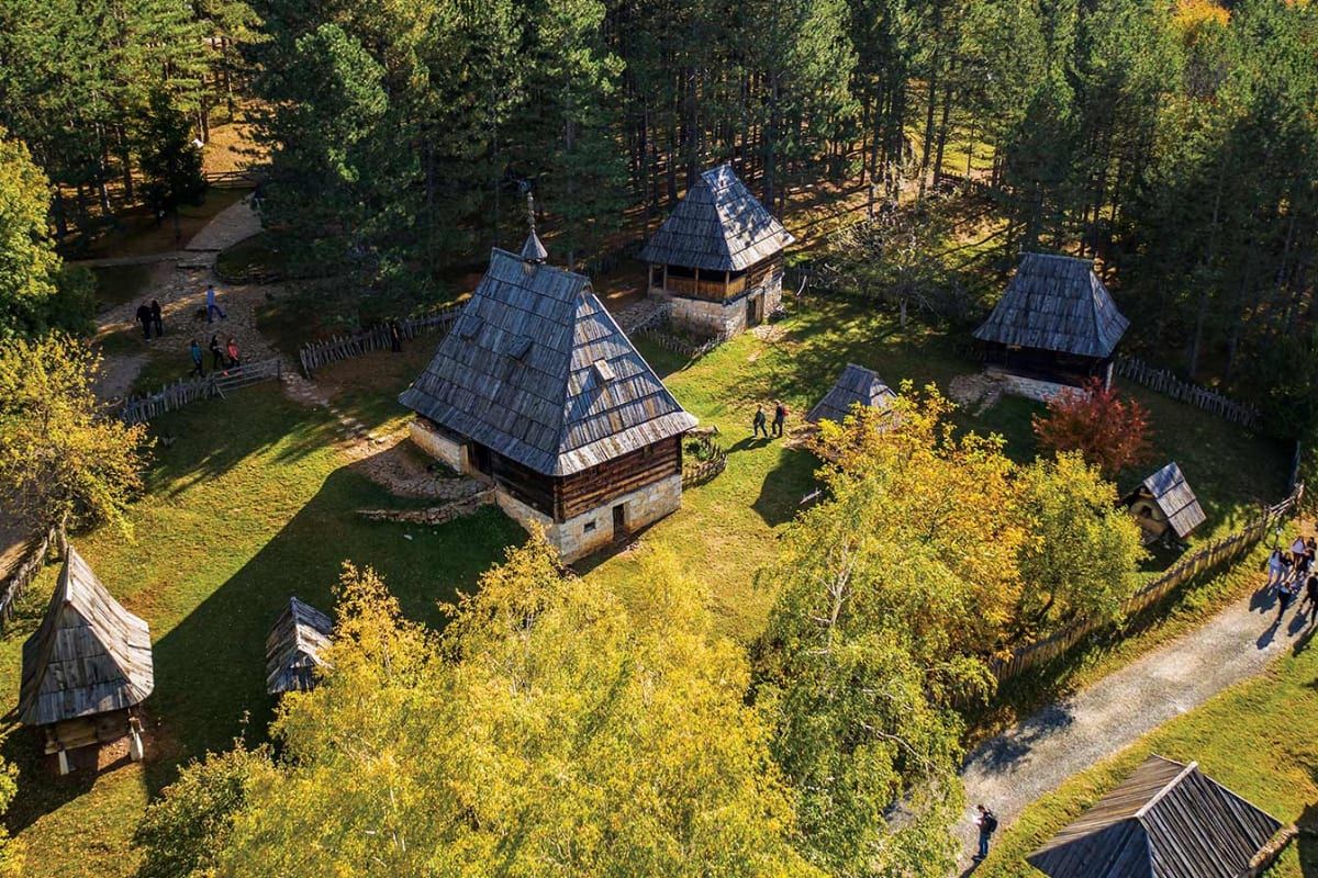 Traditional wooden log houses of the Sirogojno open-air Old Village museum among pine and autumn woodland.